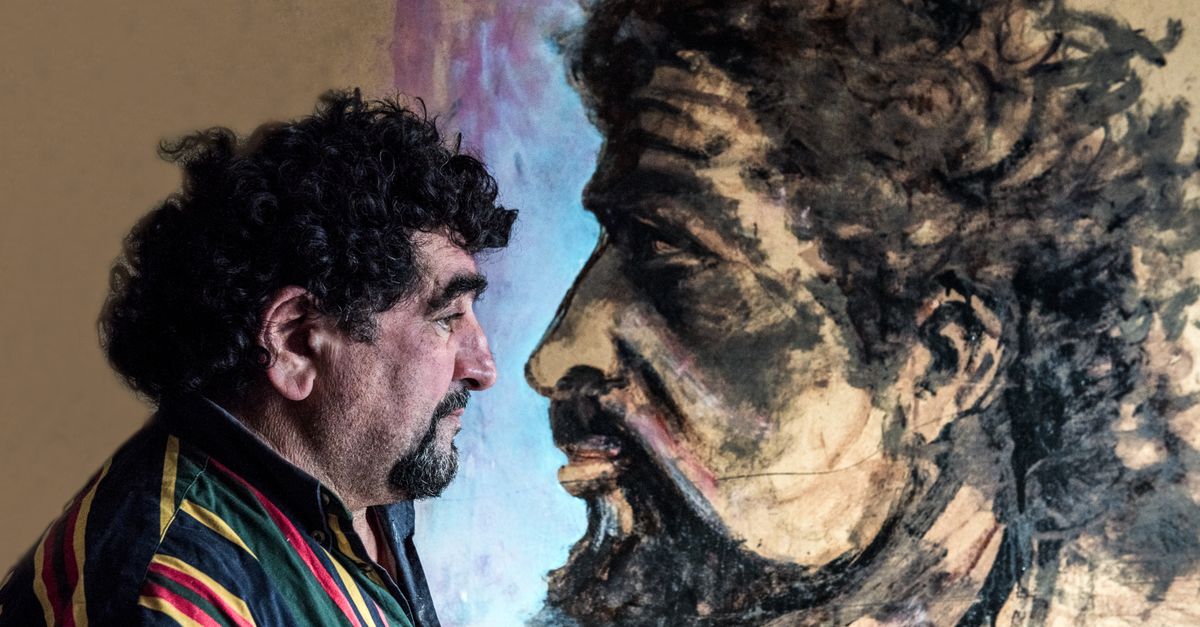 Side profile of a man with beard looking at an artistic painted portrait on a wall.